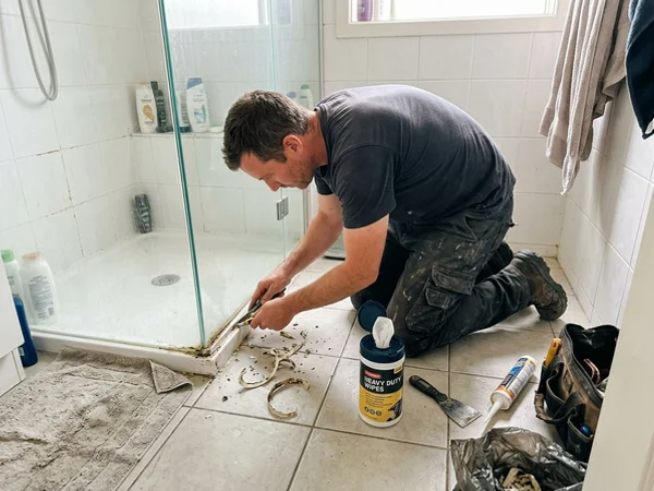 Old mouldy silicone being cut out at a shower panel base