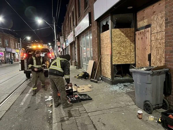 Shattered restaurant entrance door boarded on Queen West at night